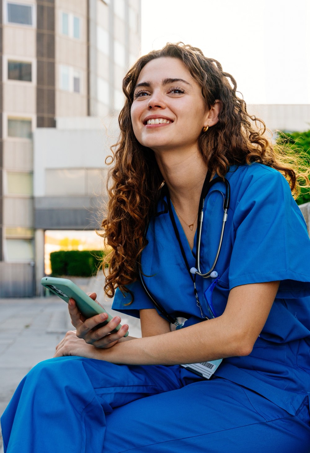 A smiling nurse in blue scrubs holding her phone